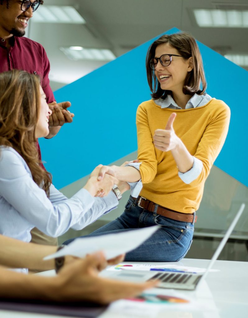 Group of young coworkers interacting around a table and handshaking in the office