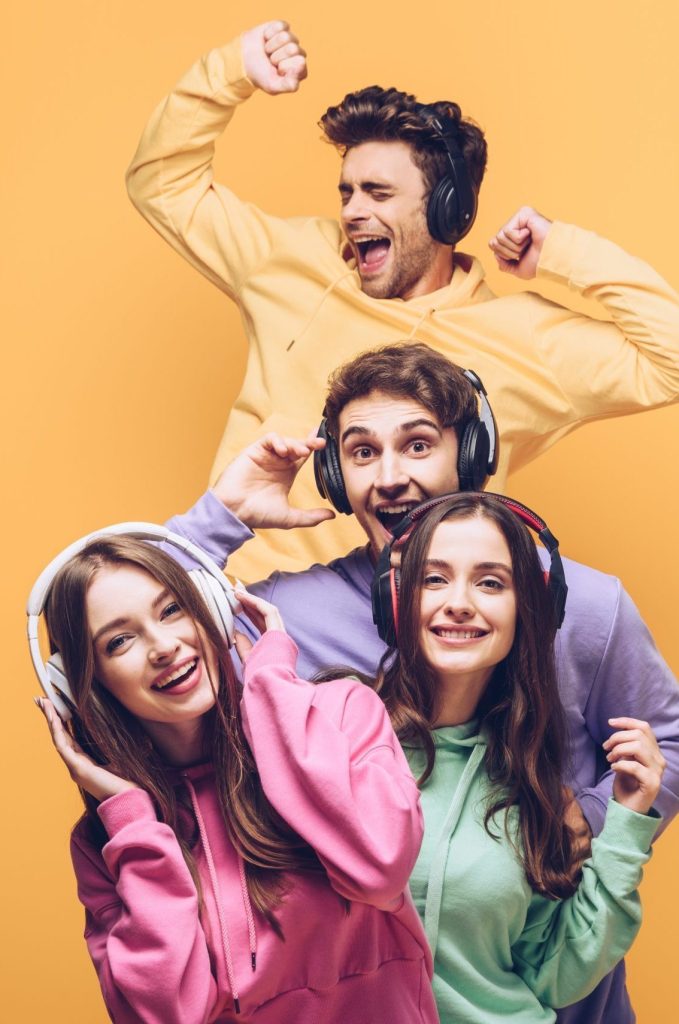 emotional friends listening music in headphones and dancing together, isolated on yellow