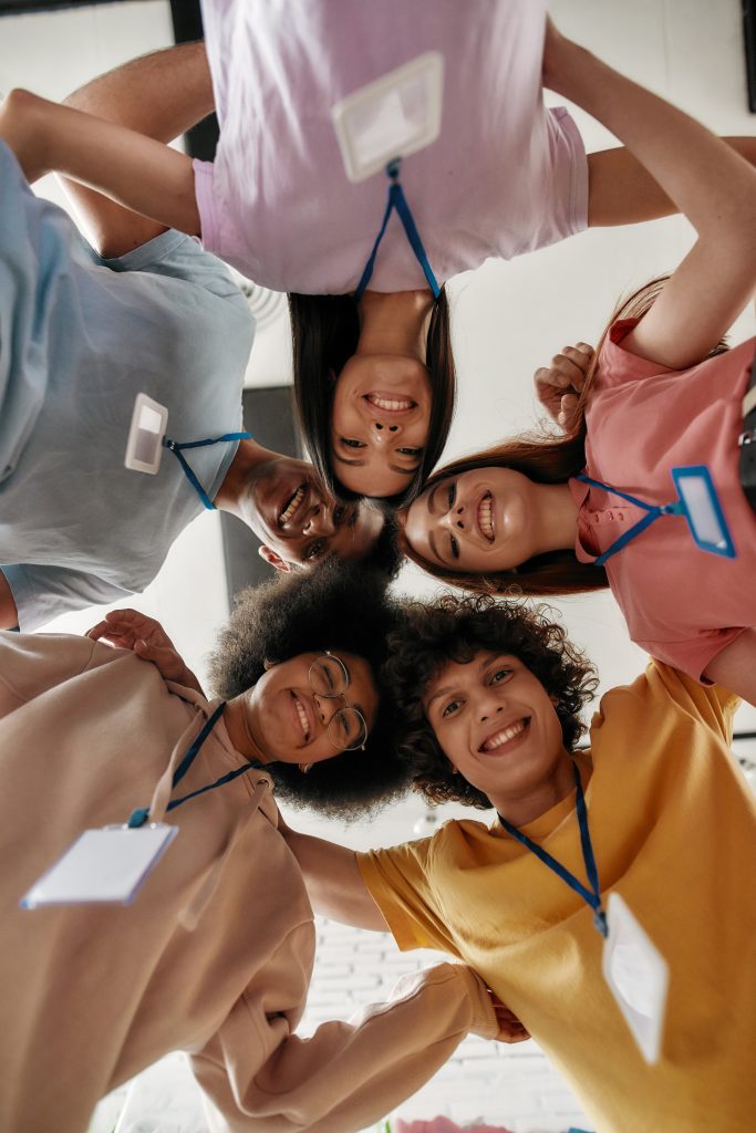 Diverse young volunteers smiling, standing in circle joined and looking down at camera